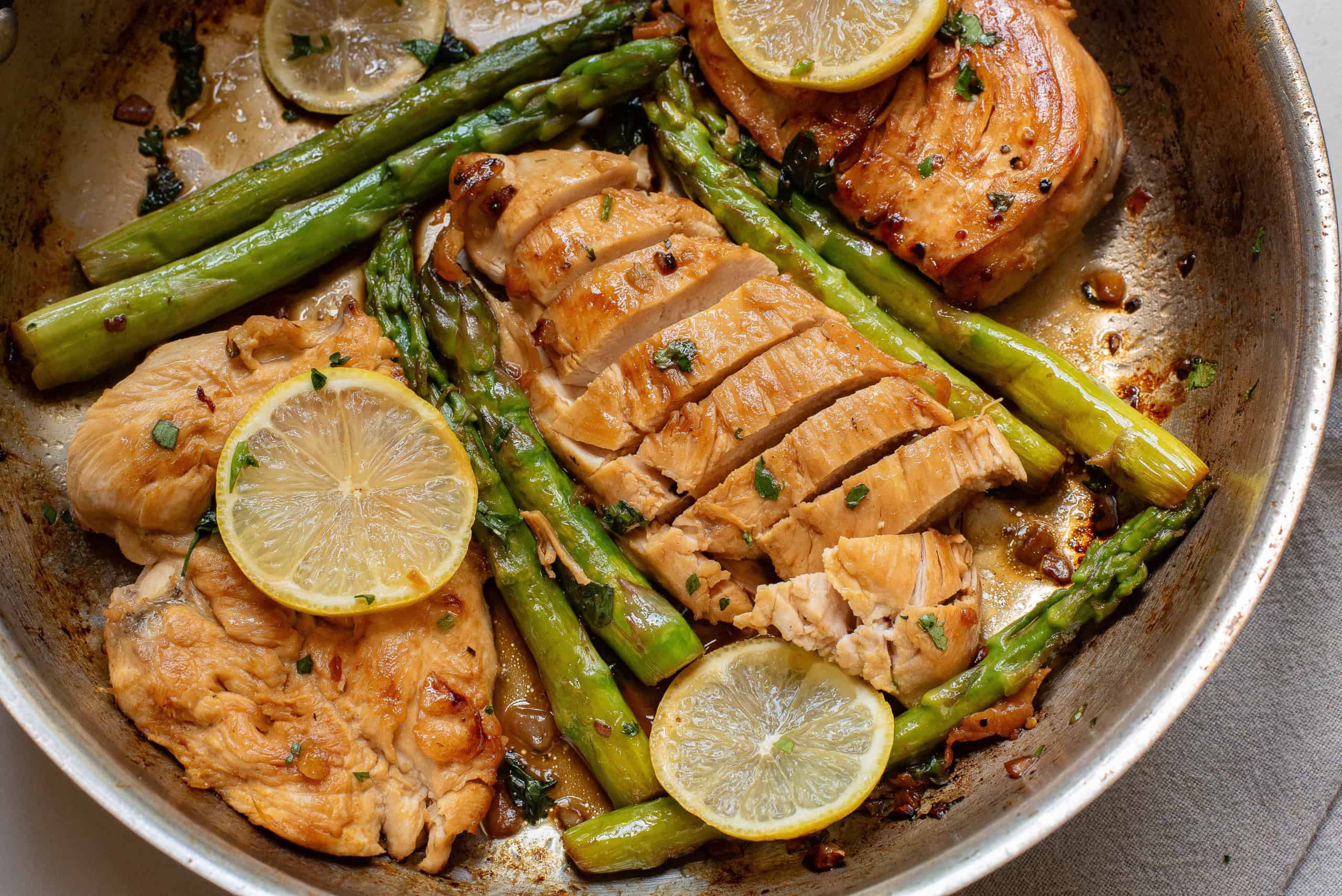 Closeup of chicken with lemon butter and asparagus in a skillet.
