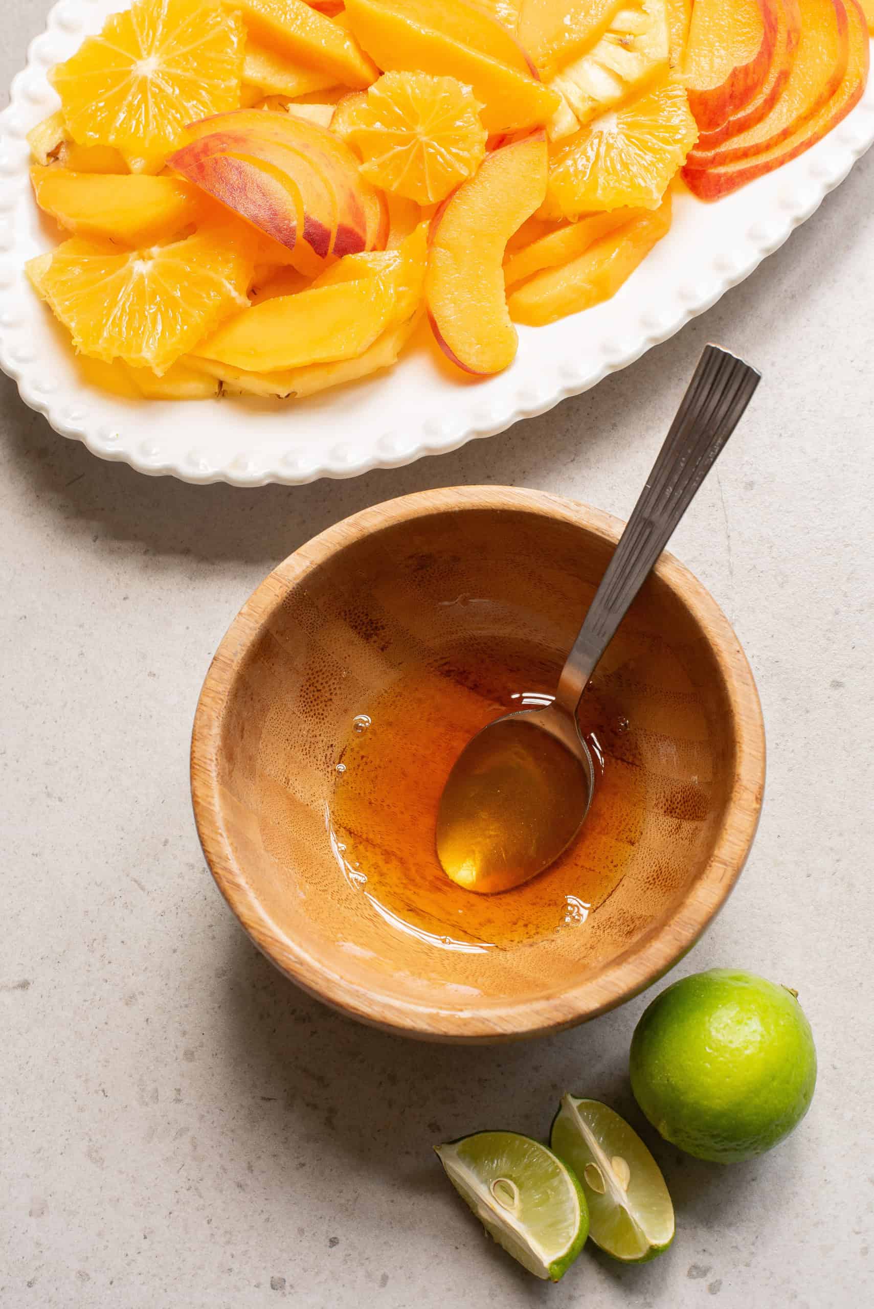 Overhead view of preparing lime honey mint dressing in wooden bowl with a spoon in it.
