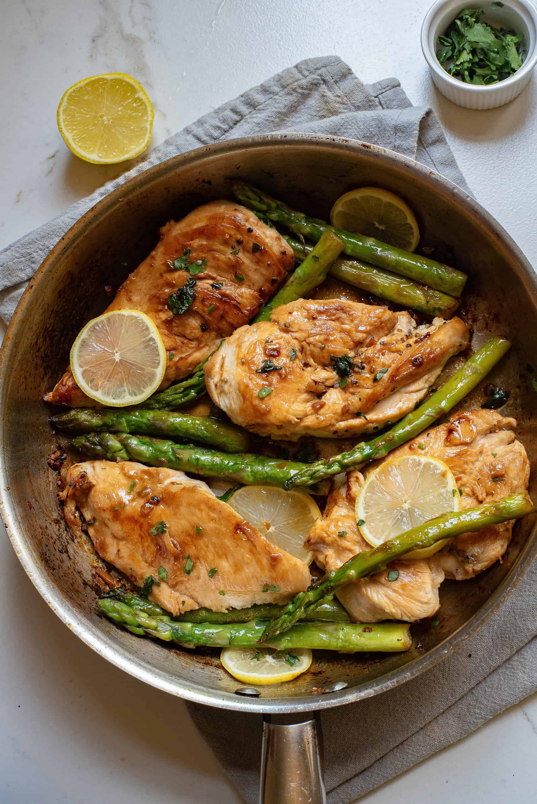 Overhead view of lemon butter chicken and asparagus in a skillet.