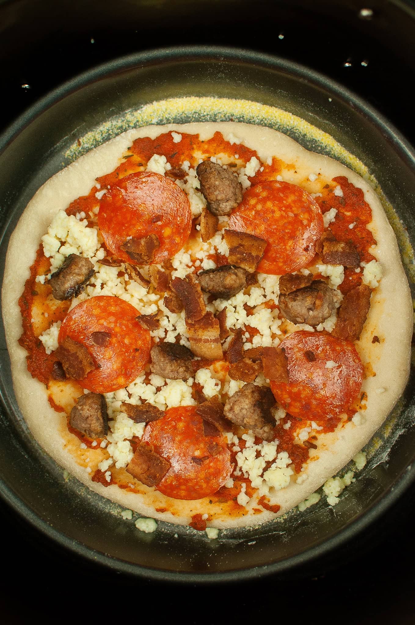 Overhead view of pizza with toppings in air fryer basket.