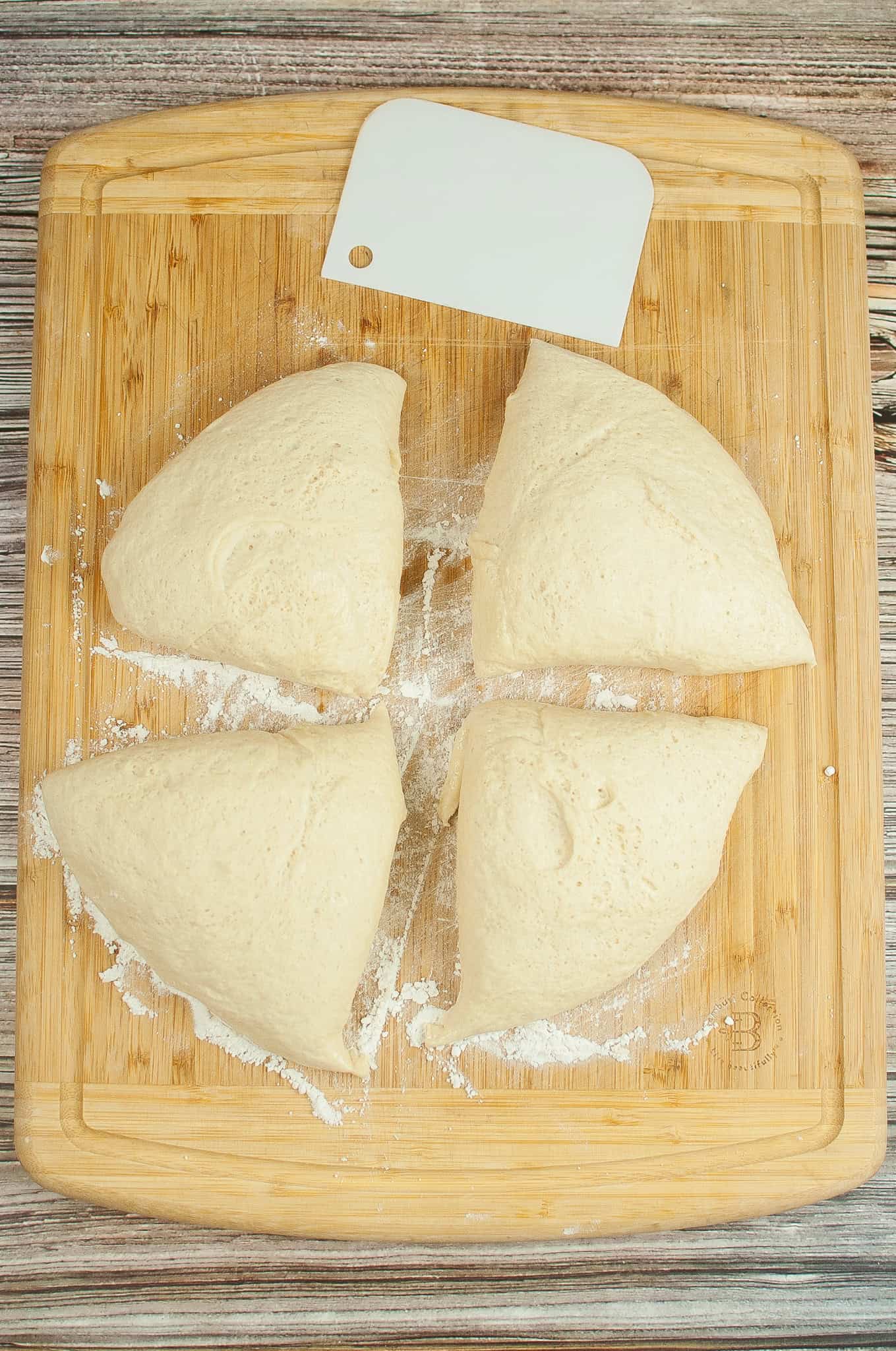 Overhead view of pizza dough cut into 4 sections on a cutting board.