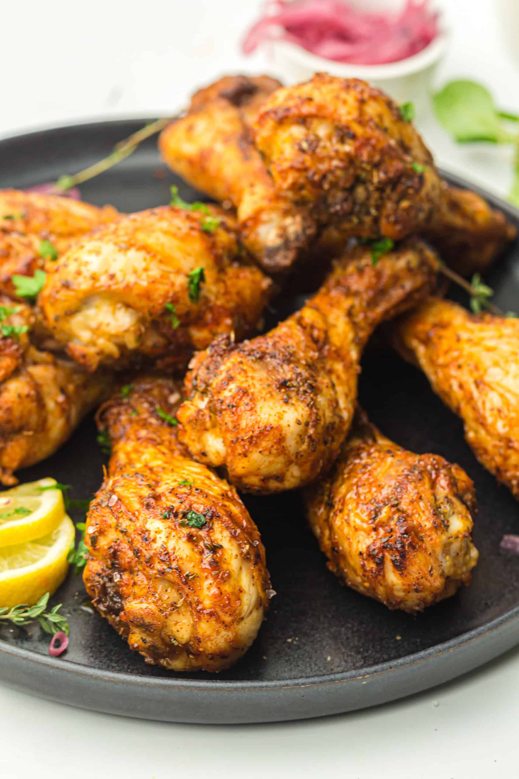 Seasoned chicken drumsticks on a black plate.