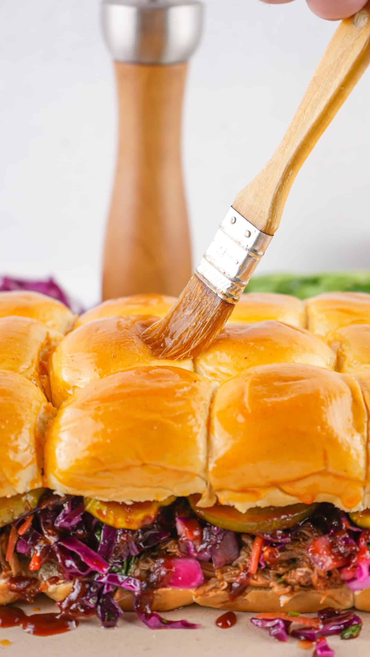 Brushing seasoned melted butter over tops of Hawaiian rolls.