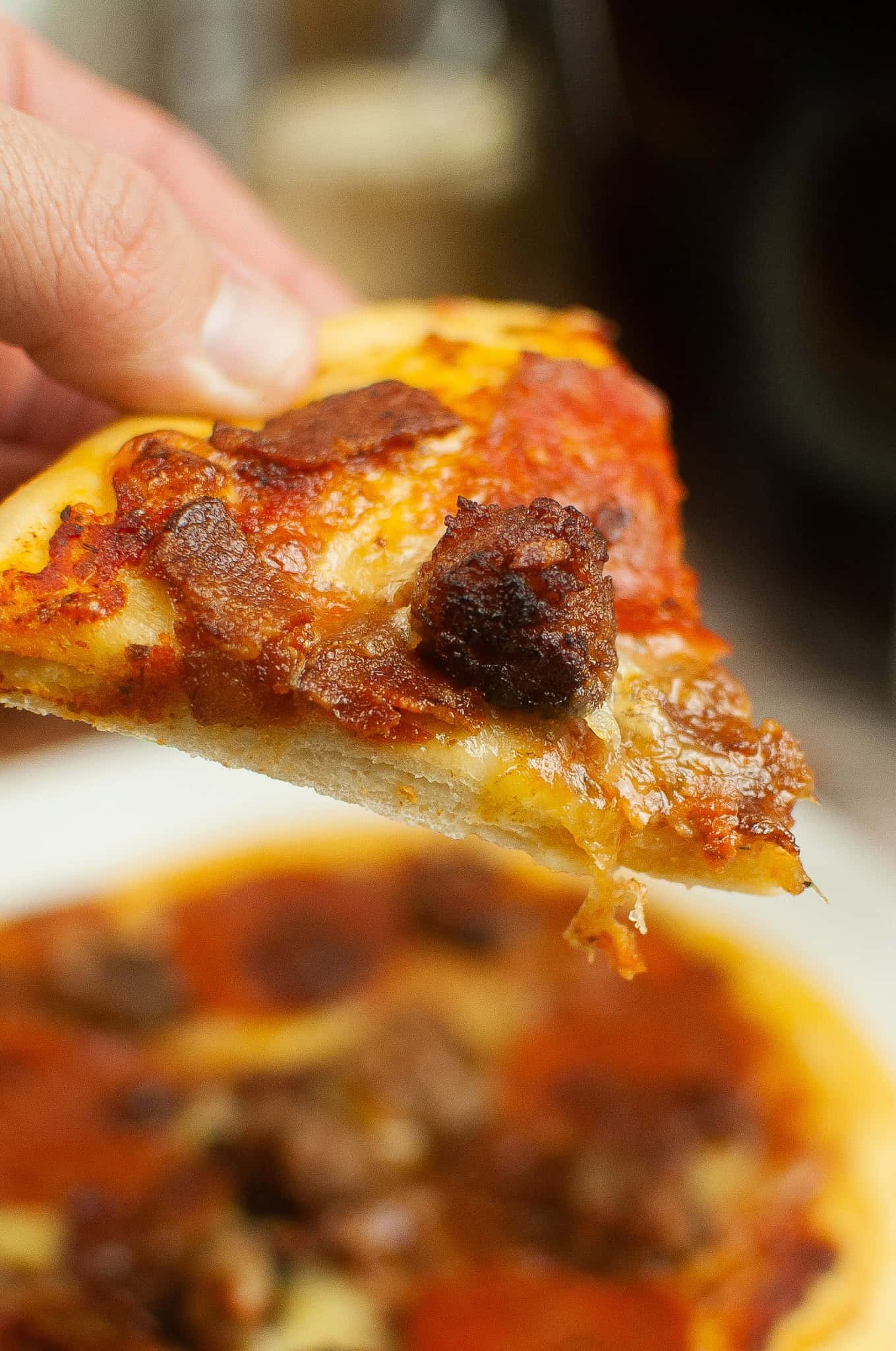 Closeup of slice of pizza with meat on it.