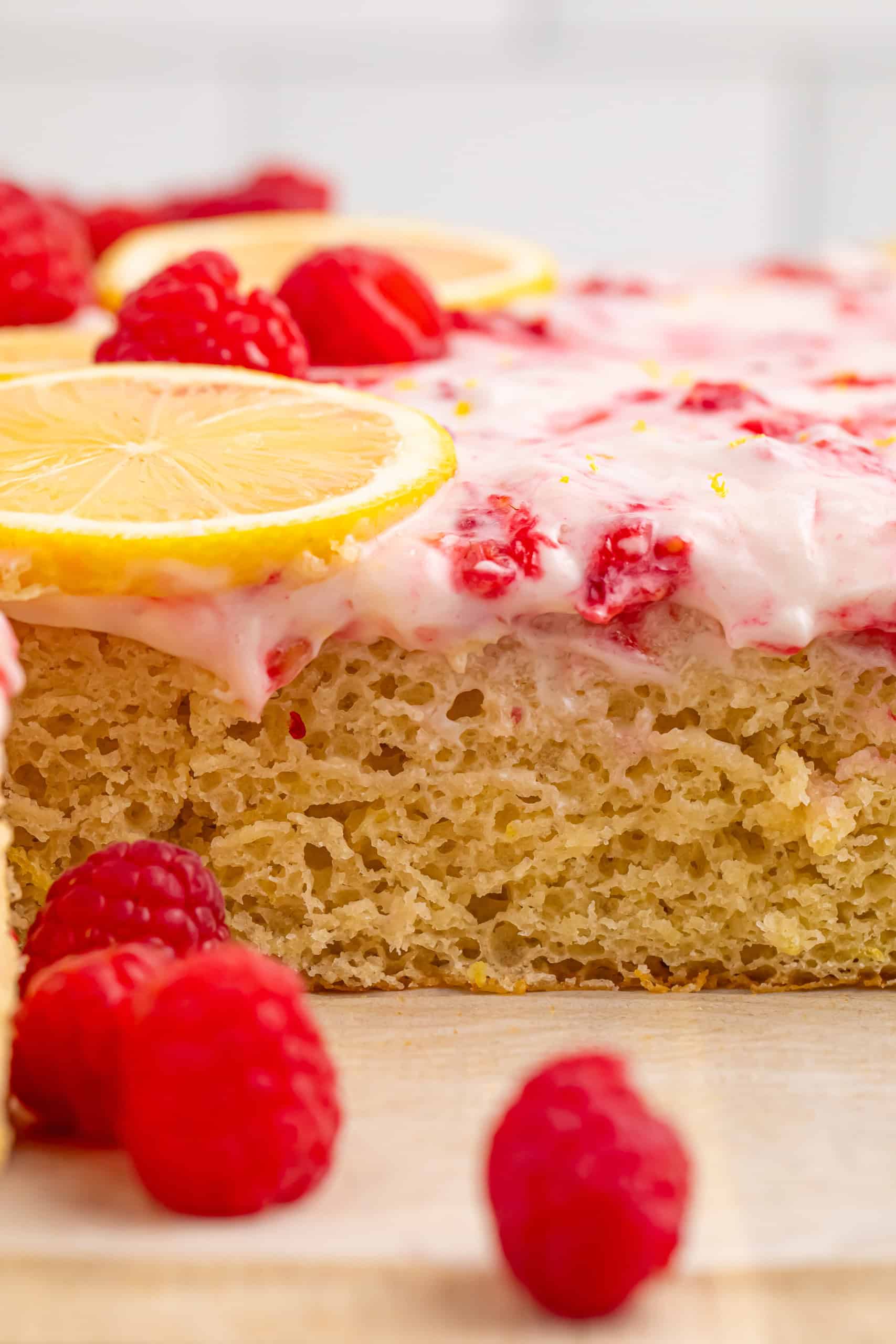 Head on photo of raspberry lemon cake on a cutting board with fresh raspberries sprinkled around it.