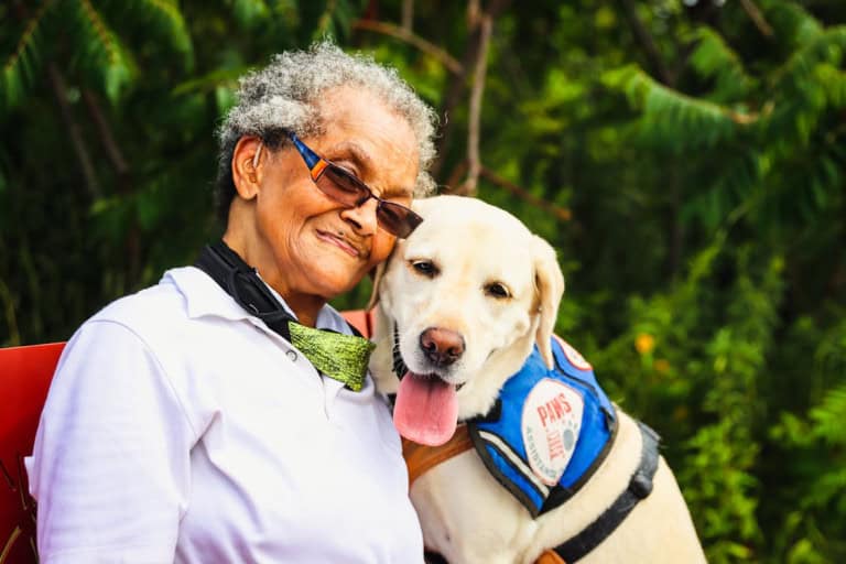 Elderly person sitting with yellow lab therapy dog.