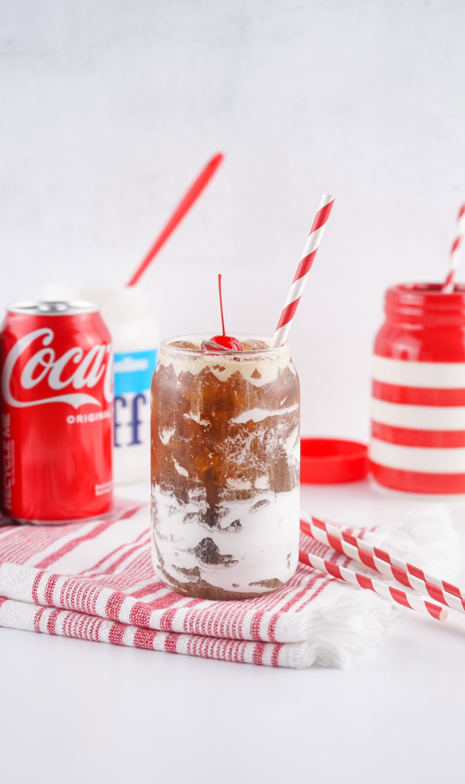 Fluffy coke in a glass with a straw with coke and fluff behind it.