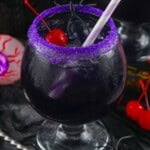 purple people eater cocktail with a purple sugar rim and a Maraschino cherry in it