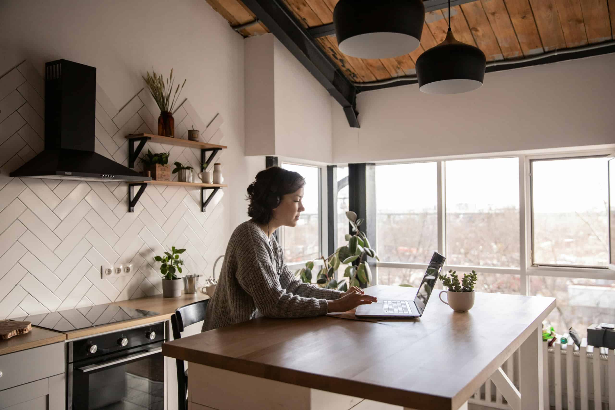 Lady in kitchen working on laptop at counter.