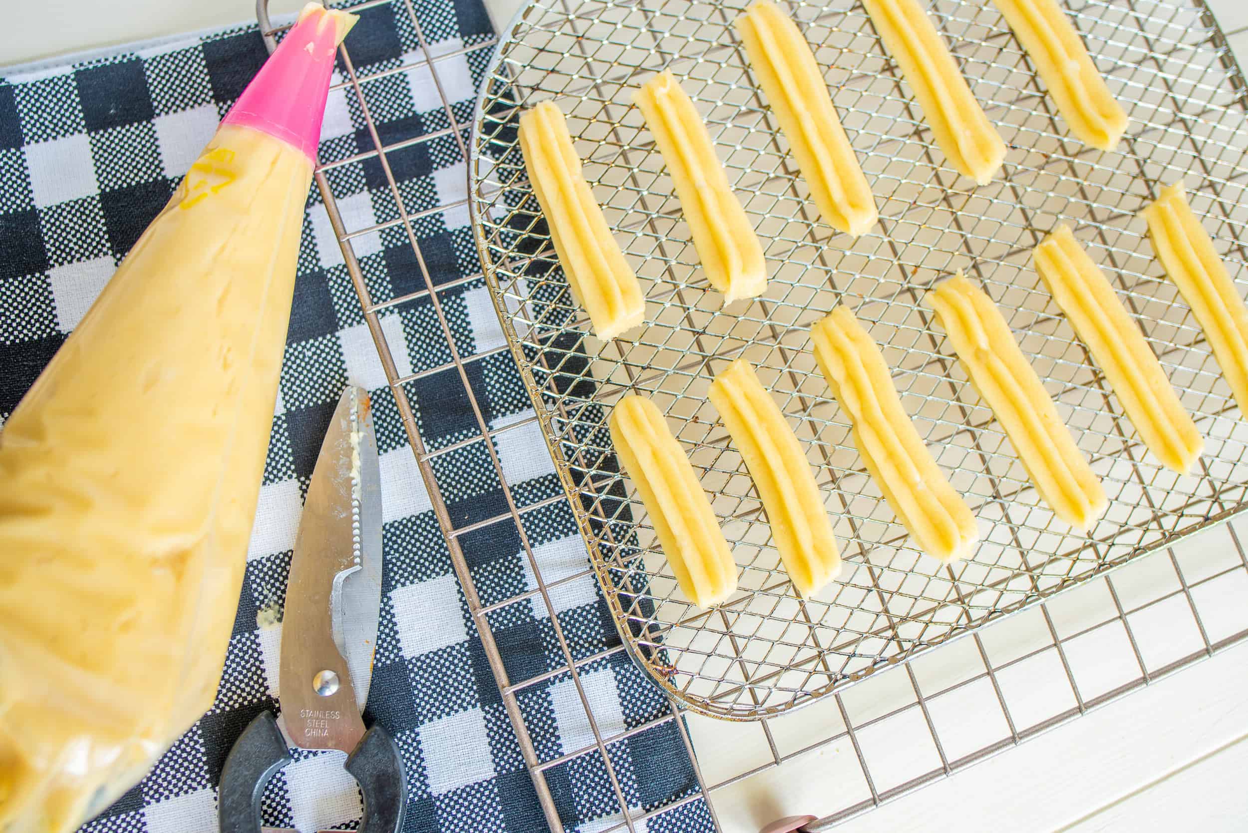 Overhead view of piping churro dough onto an air fryer wire rack.