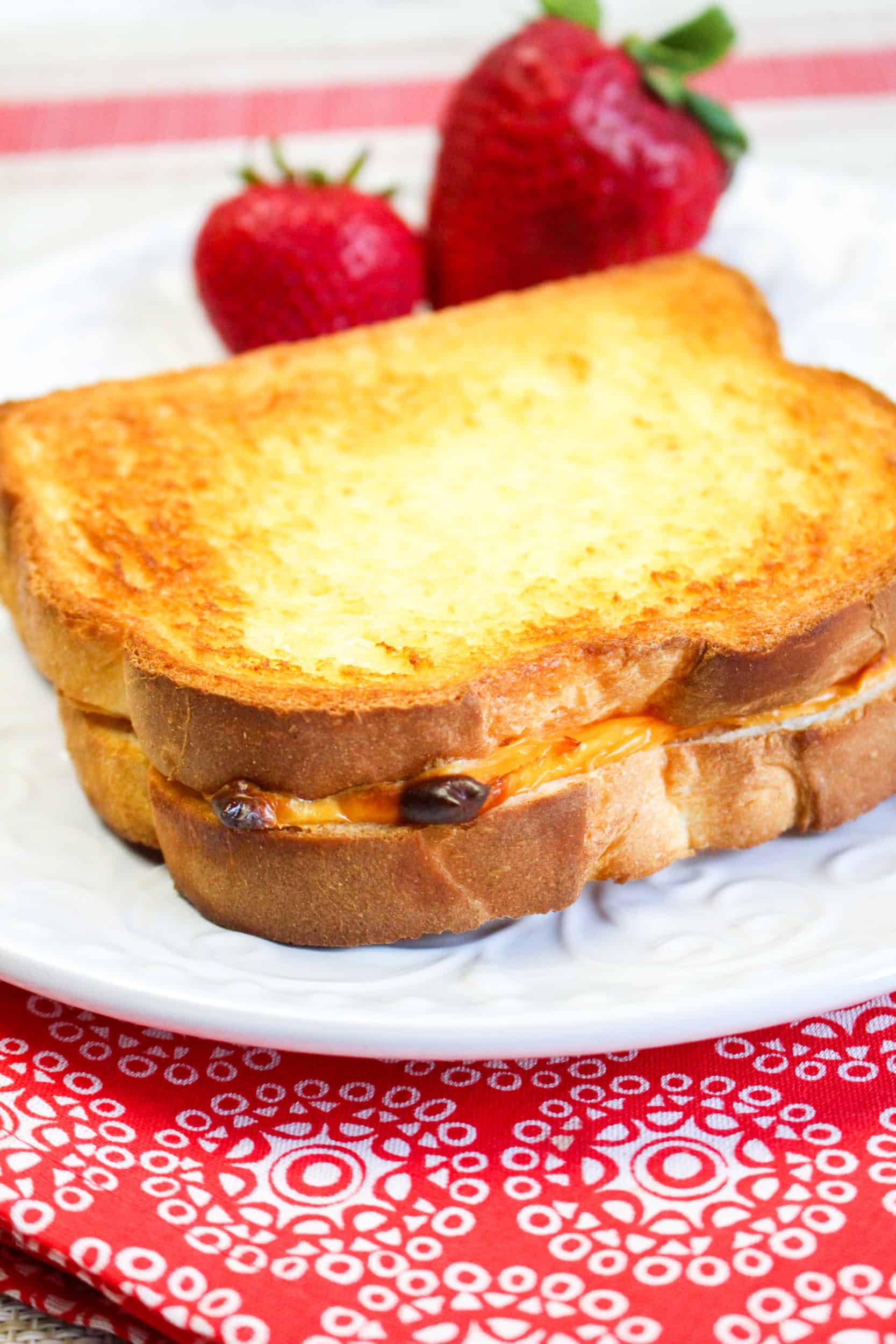 Grilled cheese sndwich n a white plate with 2 strawberries on the plate.