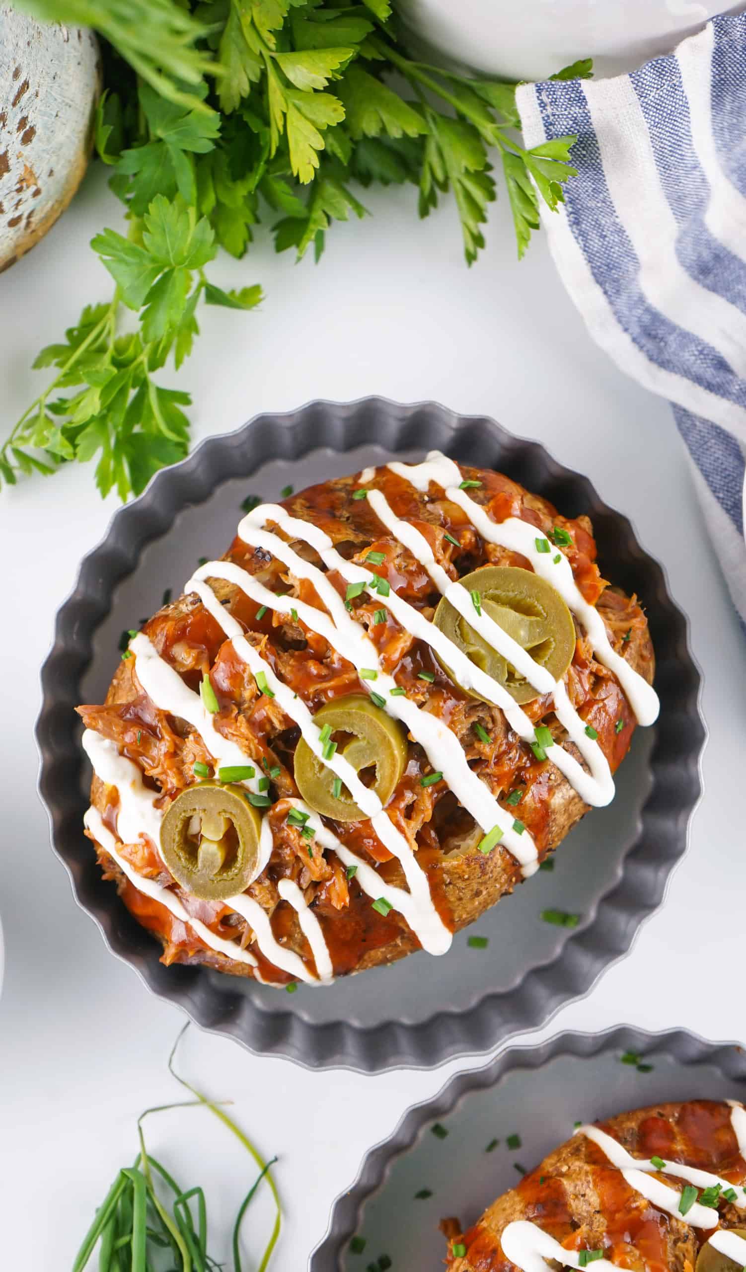 Overhead view baked potato with pulled pork, sour cream and pickled jalapenos.
