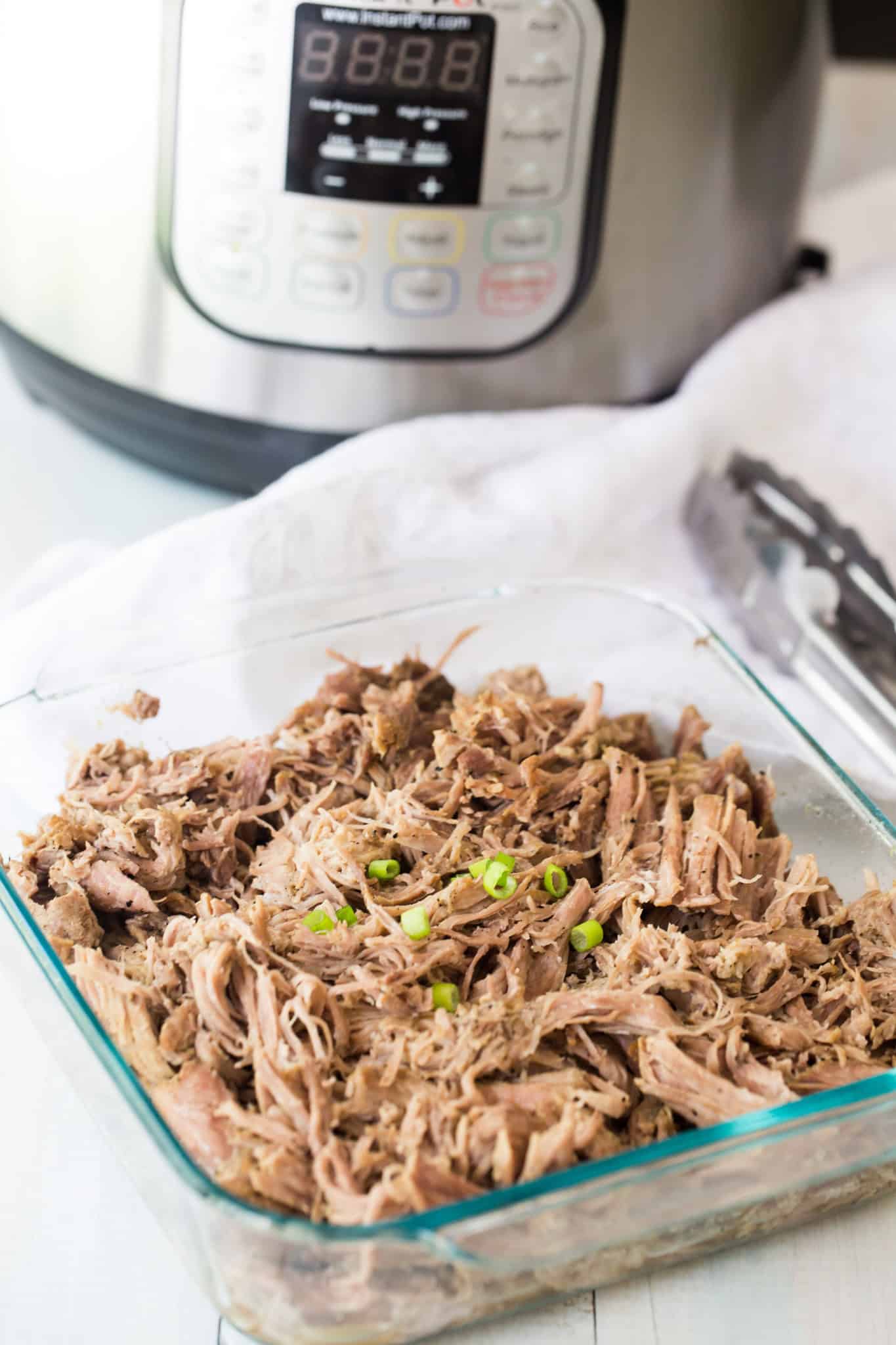 Instant Pot Pulled Pork Butt in glass dish in fornt of Instant Pot.