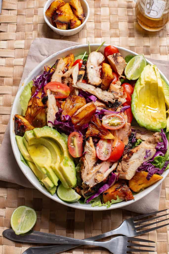 Overhead view of grilled chicken salad with avocado and grilled pineapple chunks.