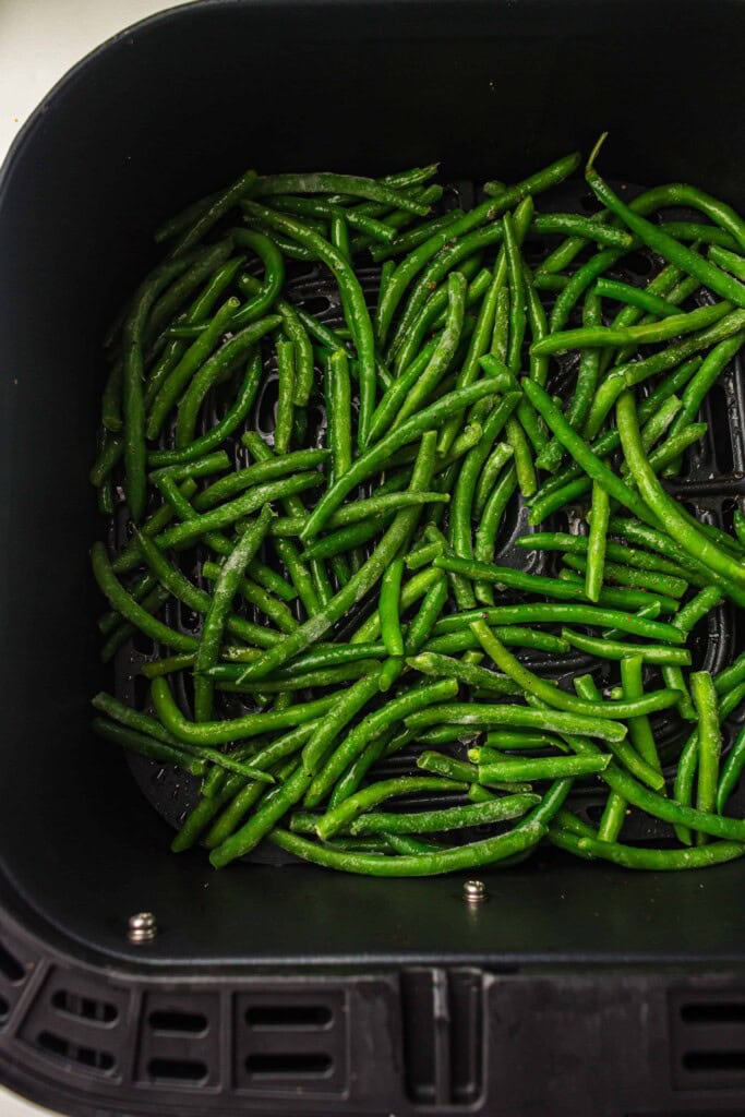 Overhead view of green beans in air fryer basket.