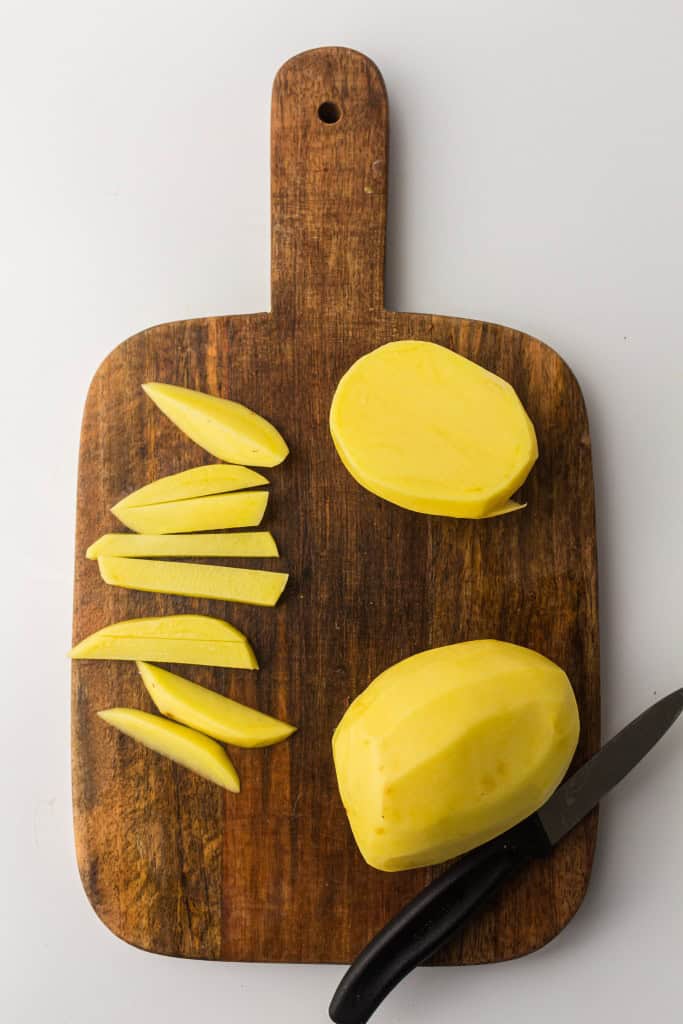 Overhead view of potatoes peeled and sliced on a cutting board.