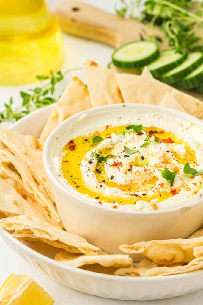 Whipped fetra dip with toasted pita chips on a white platter.