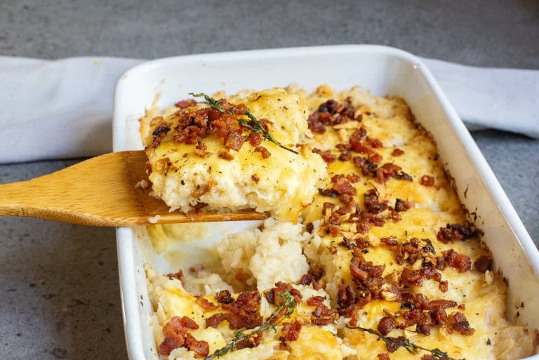 caulifower casserole scooped out of dish with a wood spatula.