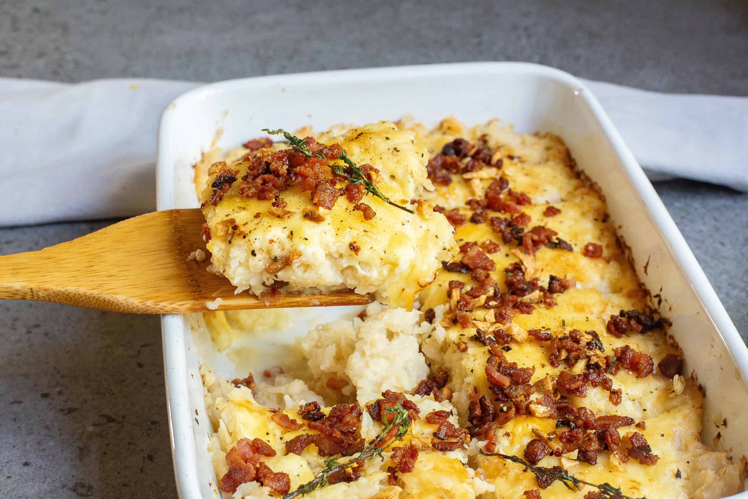 caulifower casserole scooped out of dish with a wood spatula.