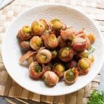 Overhead view of bacon wrapped sprouts in a white bowl.