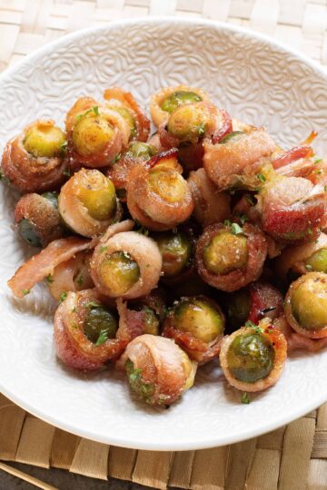 Overhead view of bacon wrapped sprouts in a white bowl.