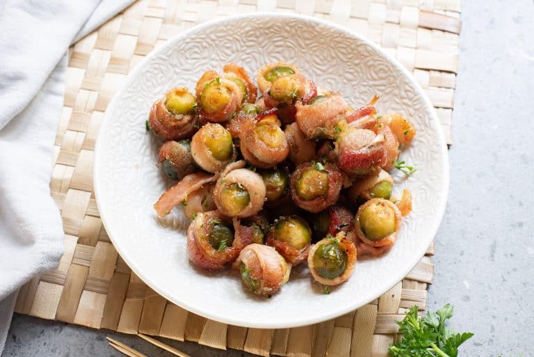Overhead view of bacon wrapped sprouts in a white bowl.