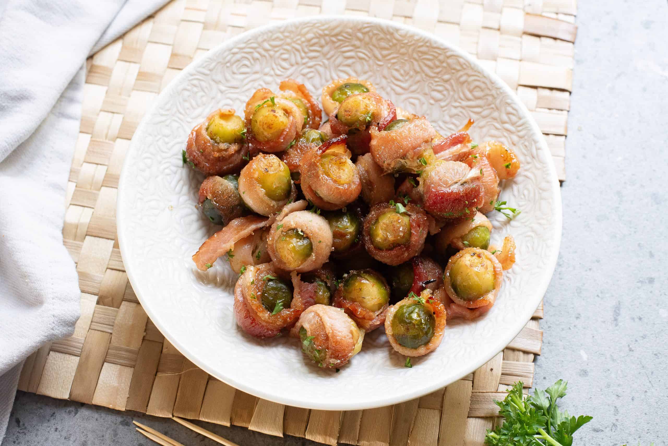 Overhead view of bacon wrapped sprouts in a white bowl.