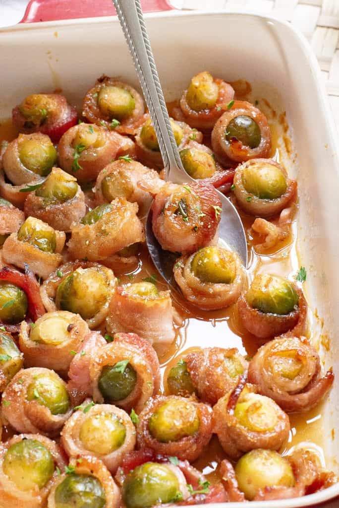 Bacon wrapped Brussels sprouts in a baking dish with a spoon.