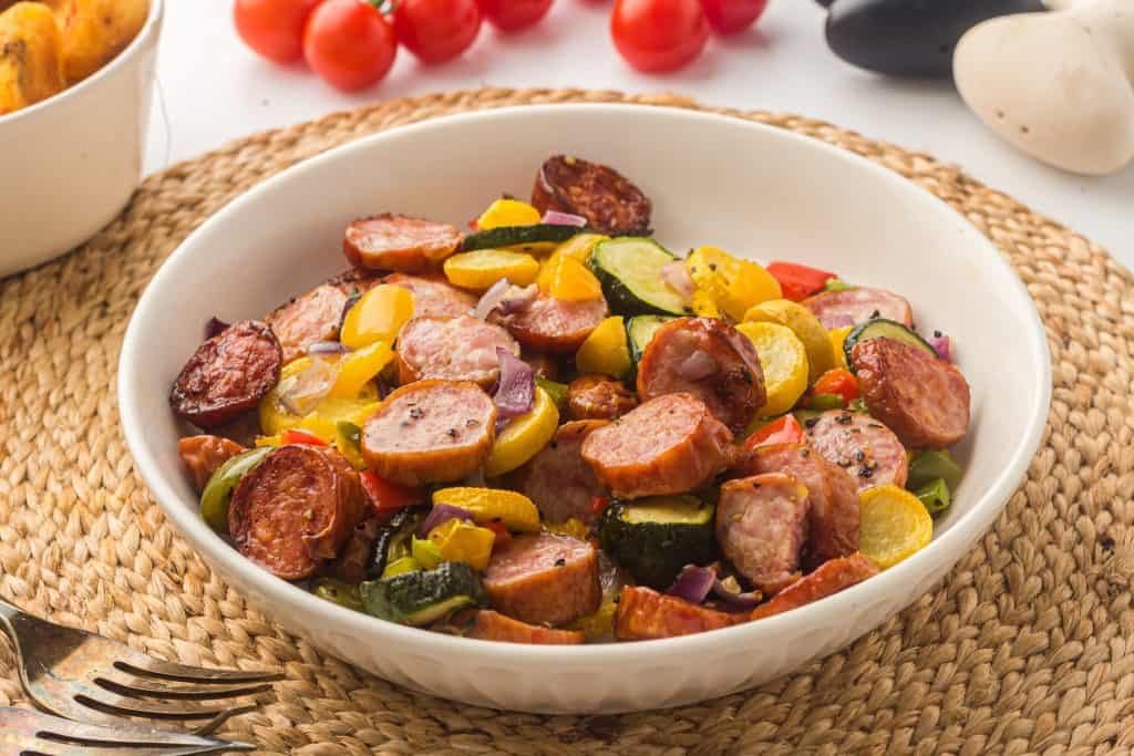 Oven roasted sausage and vegetables in a white bowl.