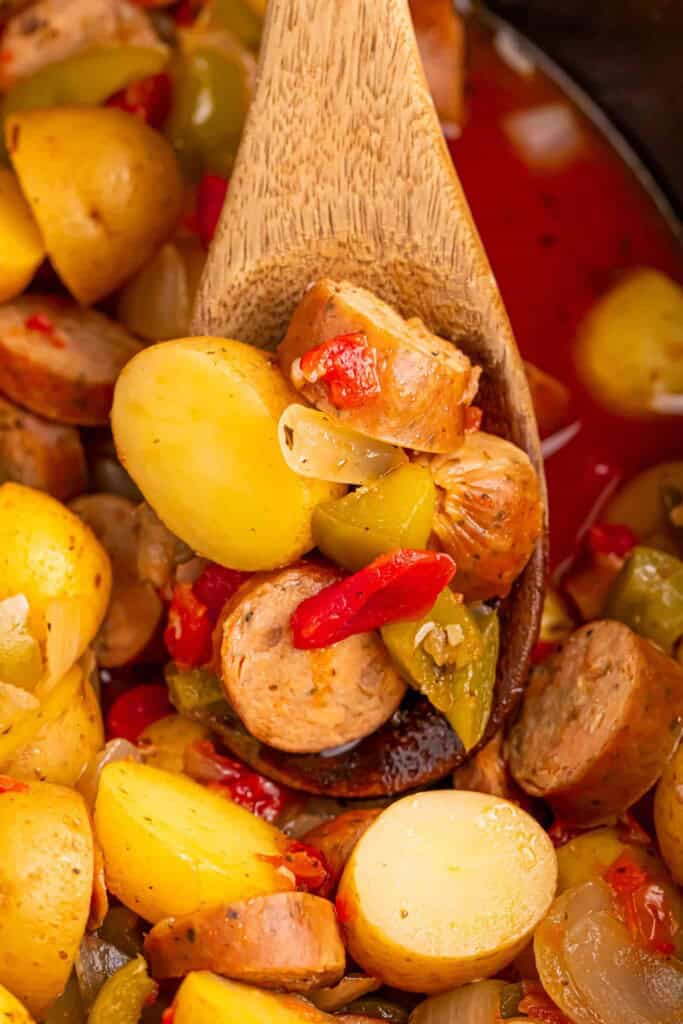 Potatoes, sausage and peppers on wood spoon in slow cooker.