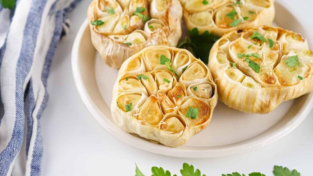 Overhead view of roasted garlic on a white plate.