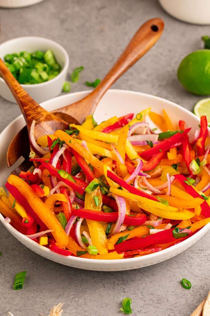 Bell pepper slaw in a white bowl with wood spoon and fork.