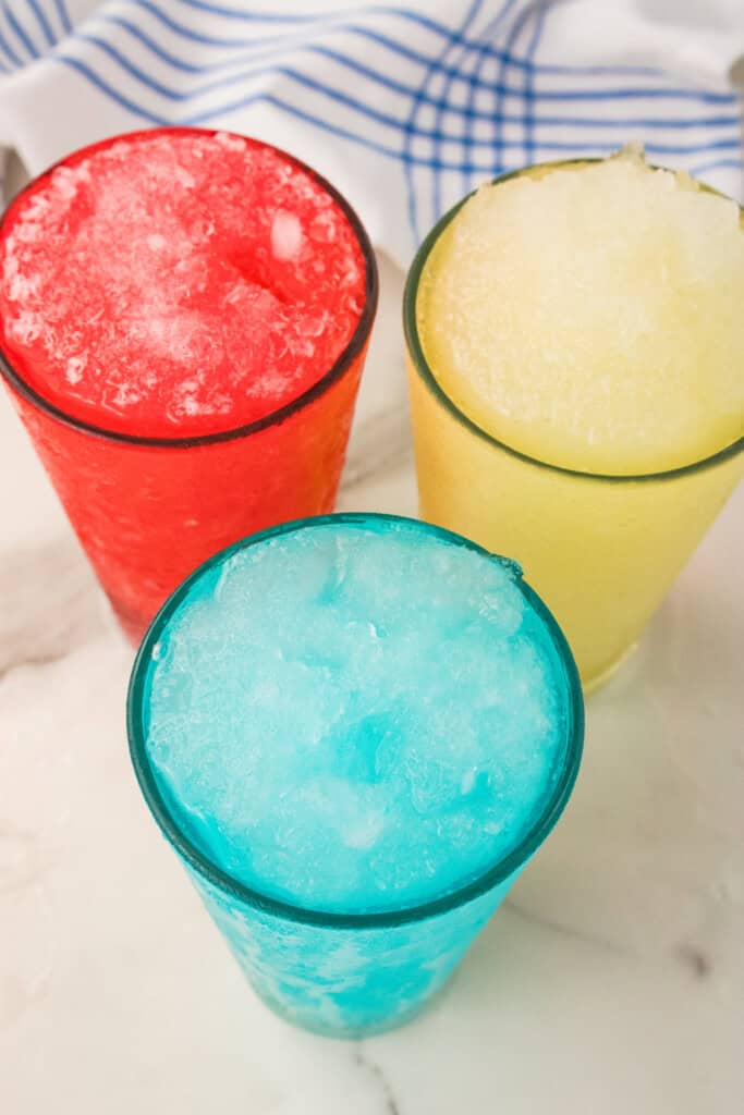 Three homemade Gatorade slushie flavors in blue, red, and yellow lined up on a marble counter