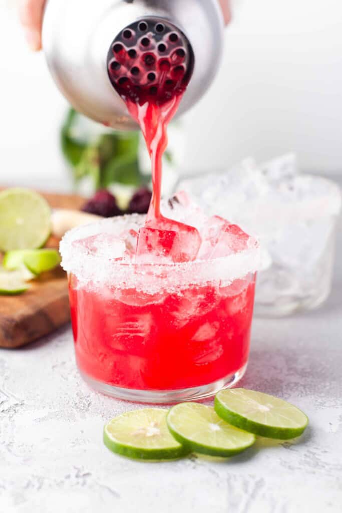 Pouring blackberry margarita out of stainless steel shaker.