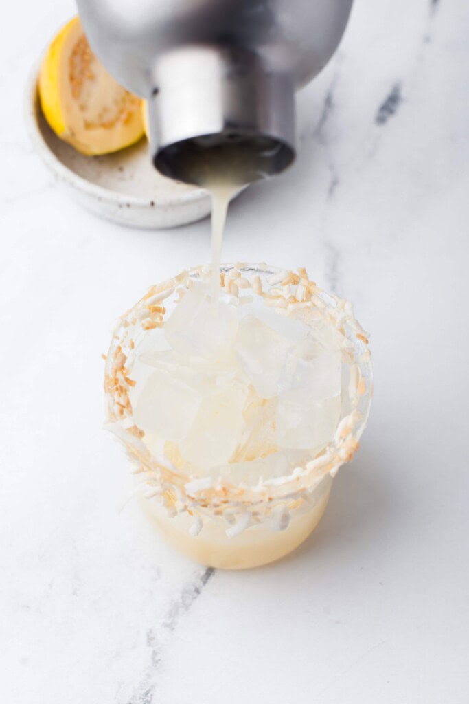 Pouring guava coconut cocktail into glass with ice.