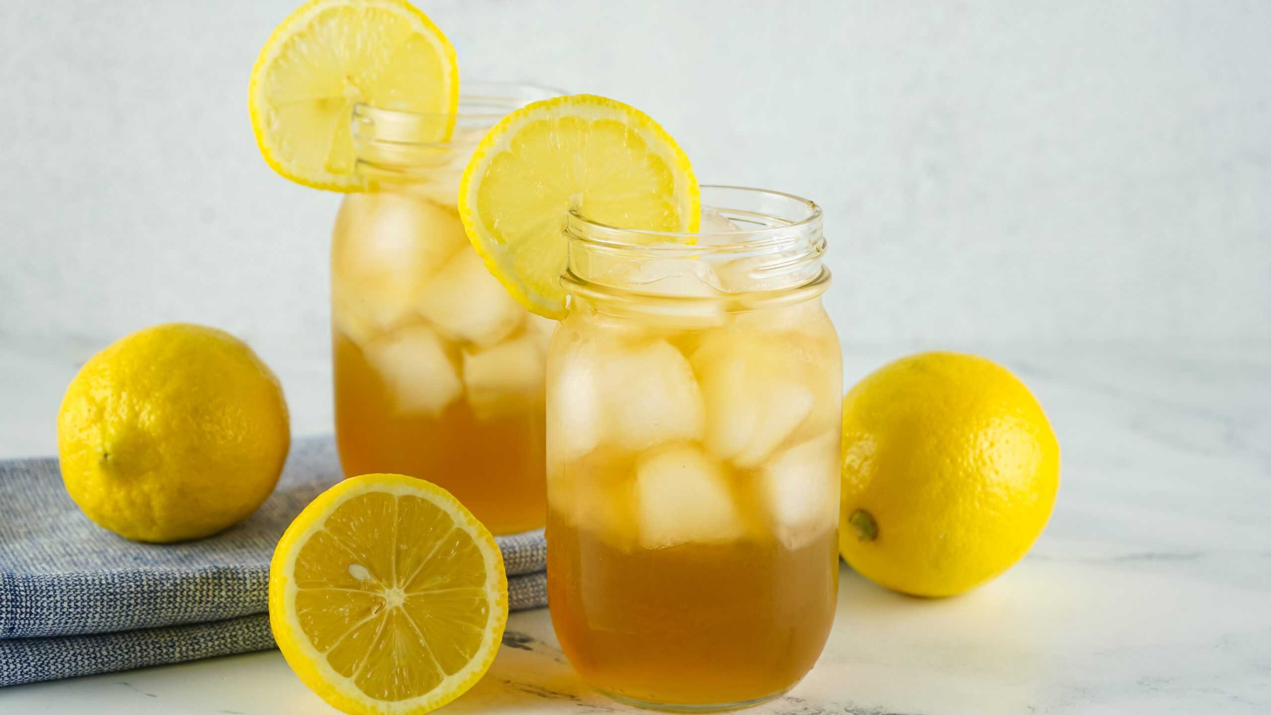 Head-on view of 2 Arnold Palmer Cocktails in glasses filled with ice with lemon slice garnishes.