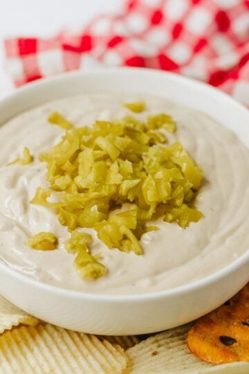 Mississippi Pot Roast Dip in a white bowl with diced up pepperocinis on top and potato chips and pretzels on the side.