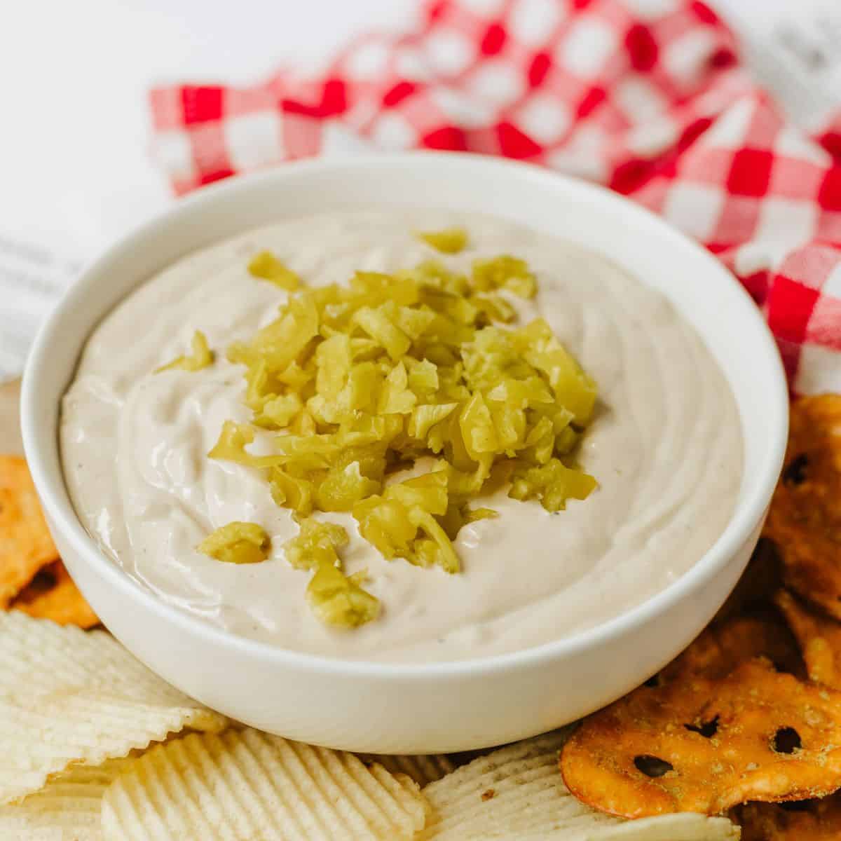 Mississippi Pot Roast Dip in a white bowl with diced up pepperocinis on top and potato chips and pretzels on the side.