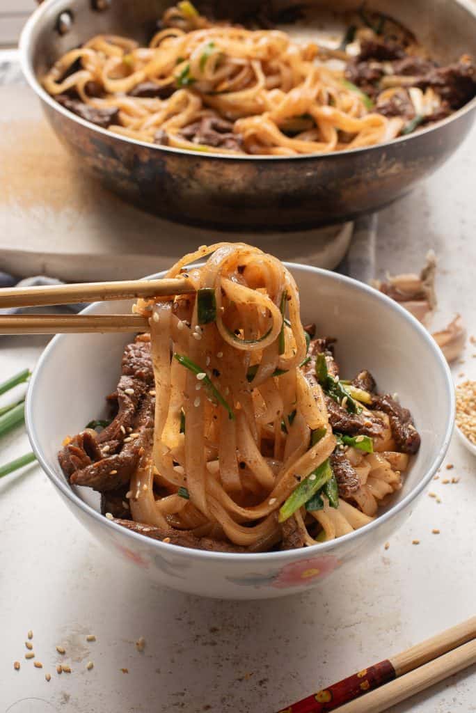 Beef chow mein in a bowl being eaten with chop sticks.