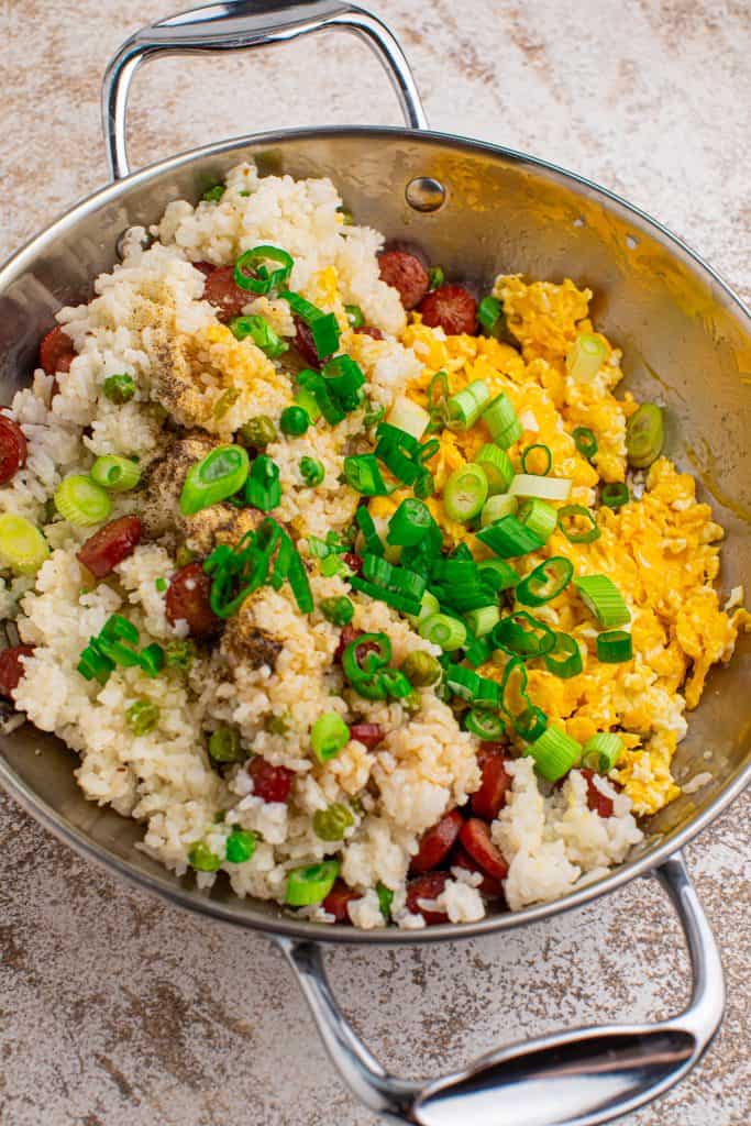 Overhead view of rice, hot dogs, scrambled eggs and sliced in green onions in a metal skillet.