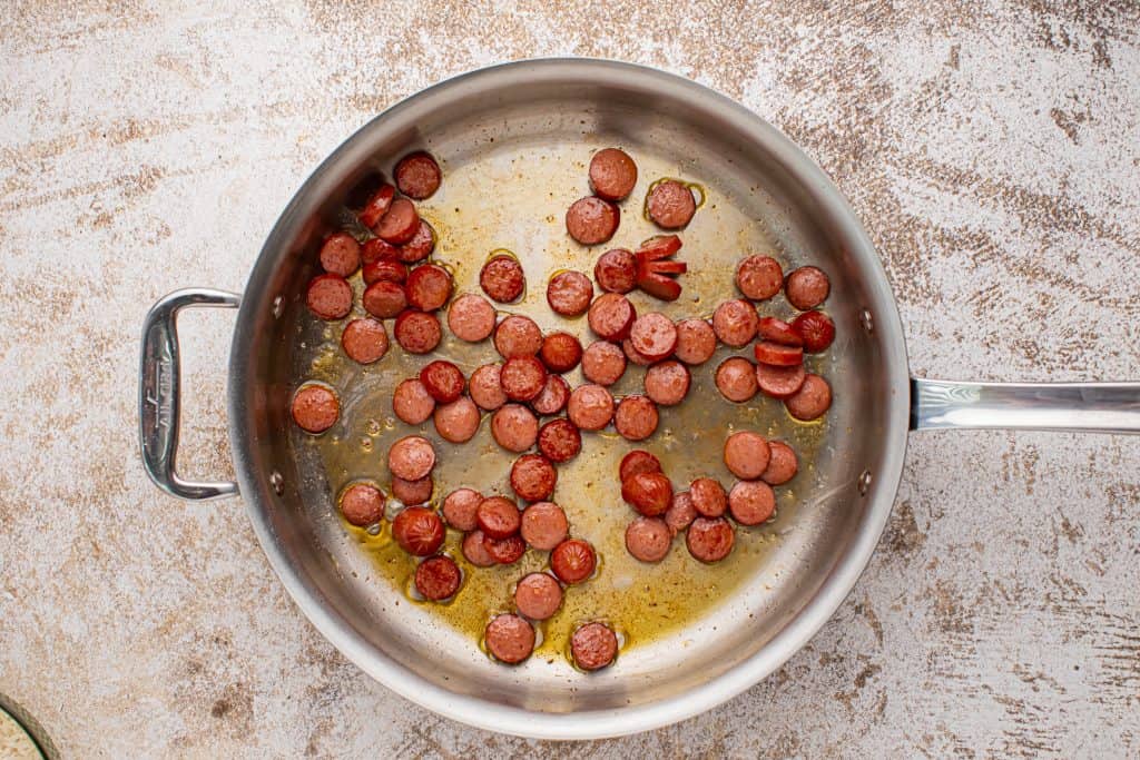 Overhead view of sliced hot dogs in a skillet.
