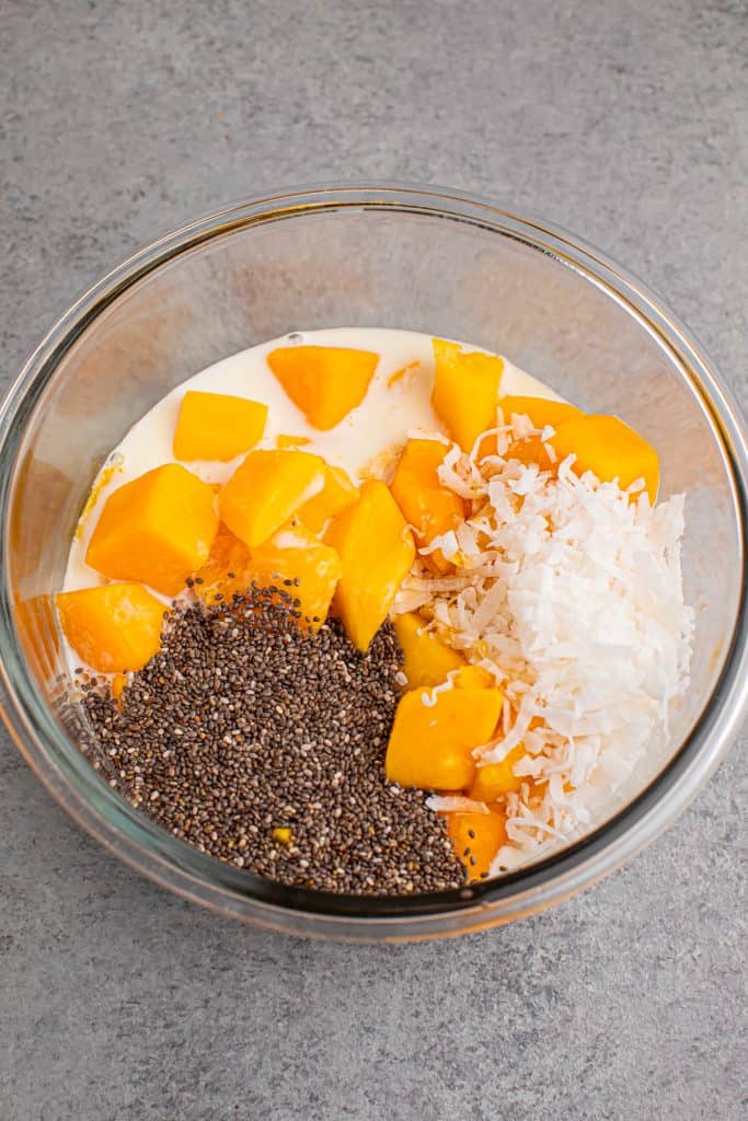 Overhead view of mango chia pudding ingredients in a glass bowl.
