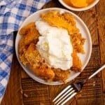 Overhead view of Peach Cobbler made with pancake mix topped with vanilla ice cream. Silver fork off to the side and blue and white checked napkin on the left side of plate.