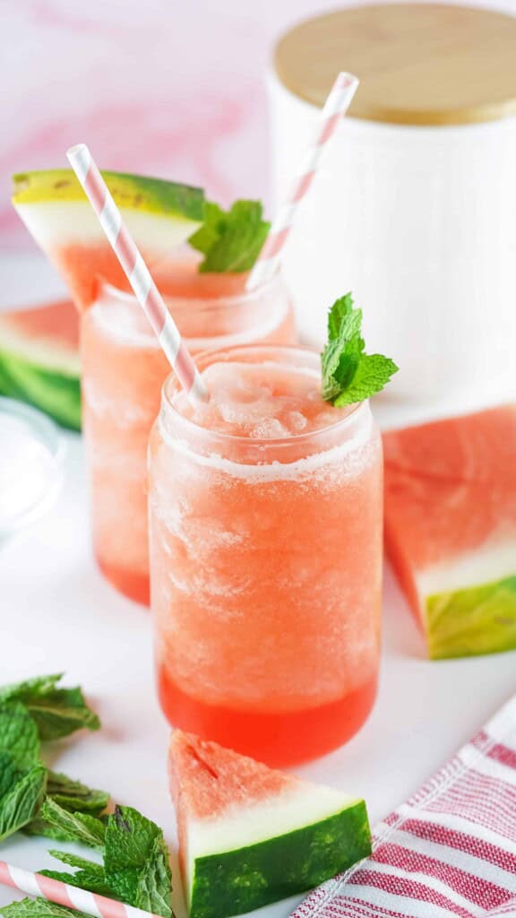 2 glasses of watermelon Agua frescos with sprigs of mint and watermelon wedges for garnish.