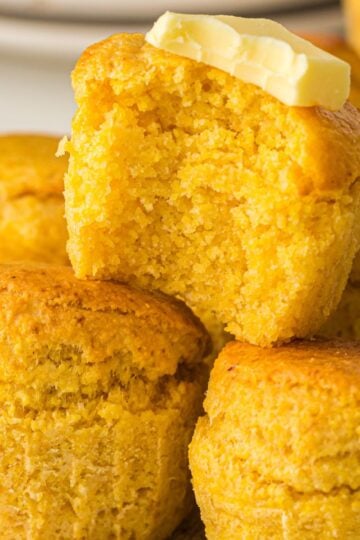 Air Fryer Cornbread Muffins stacked on top of each other. One with a bite out of it and butter on top.