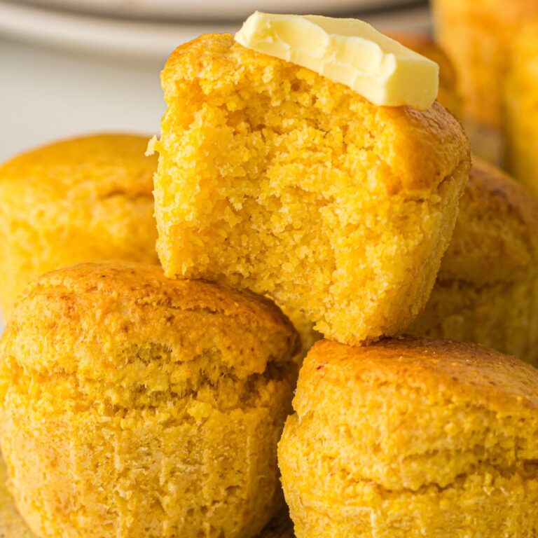 Air Fryer Cornbread Muffins stacked on top of each other. One with a bite out of it and butter on top.