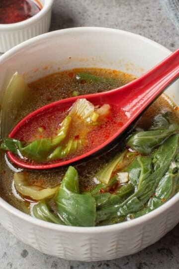 Bok Choy Soup in a white bowl with a red spoon ladle.