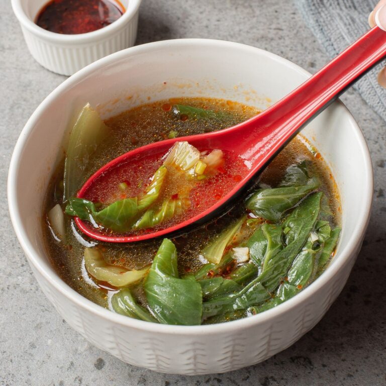 Bok Choy Soup in a white bowl with a red spoon ladle.