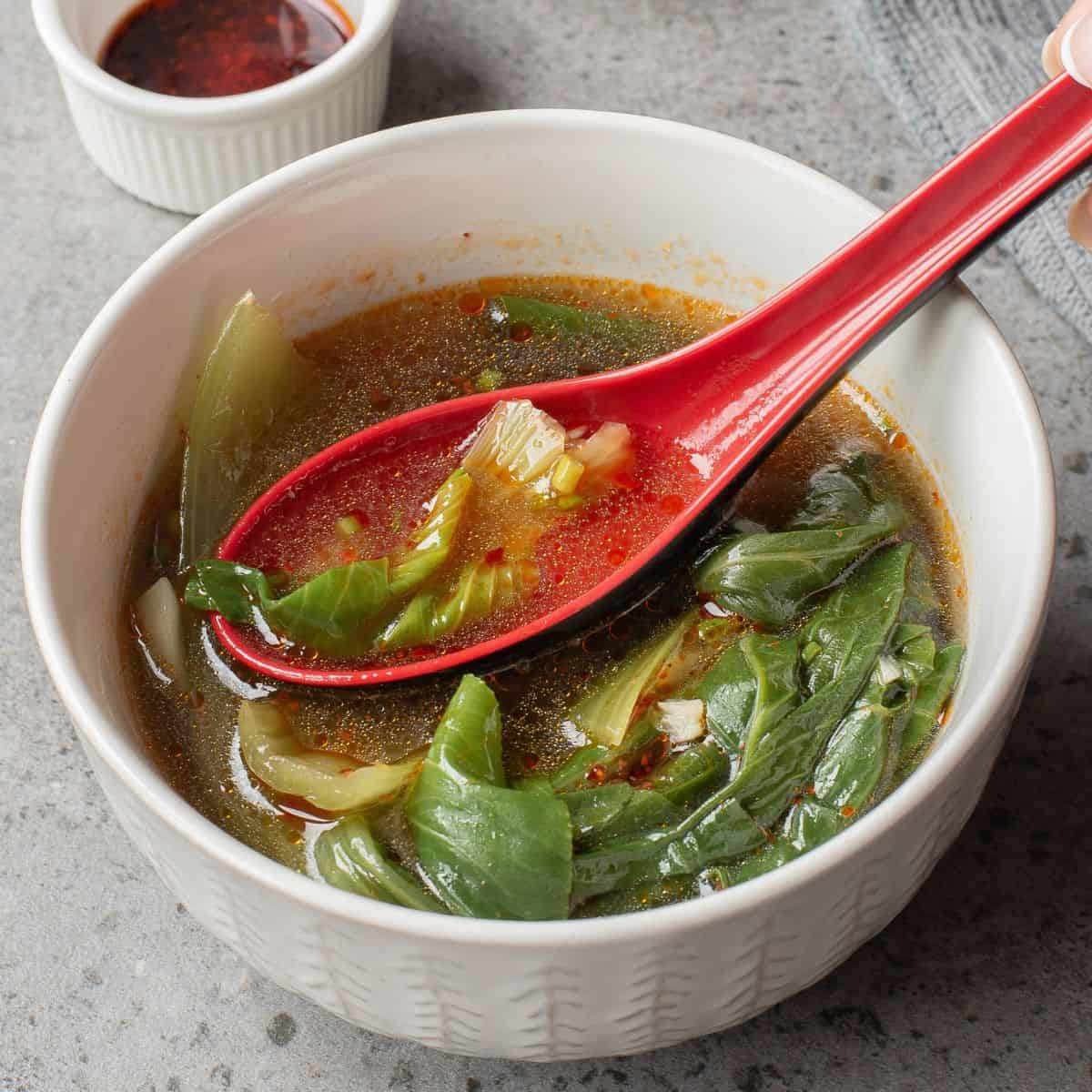 Bok Choy Soup in a white bowl with a red spoon ladle.