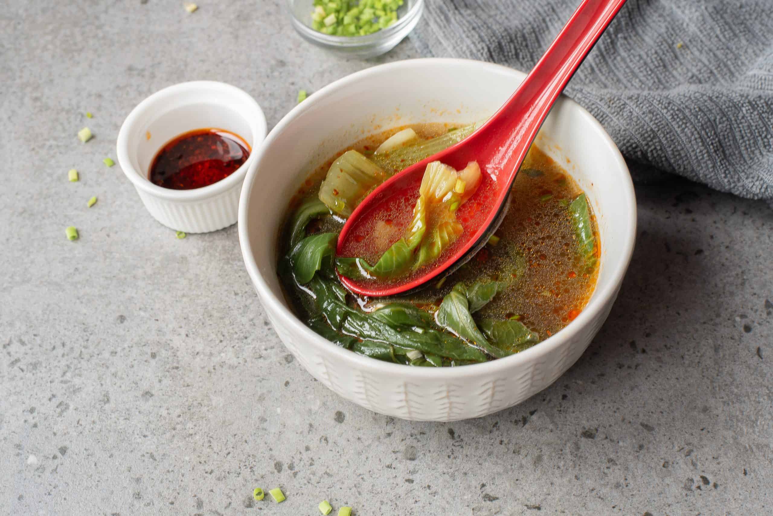 Bowl of Bok Choy Soup with red ladle spoon in it.